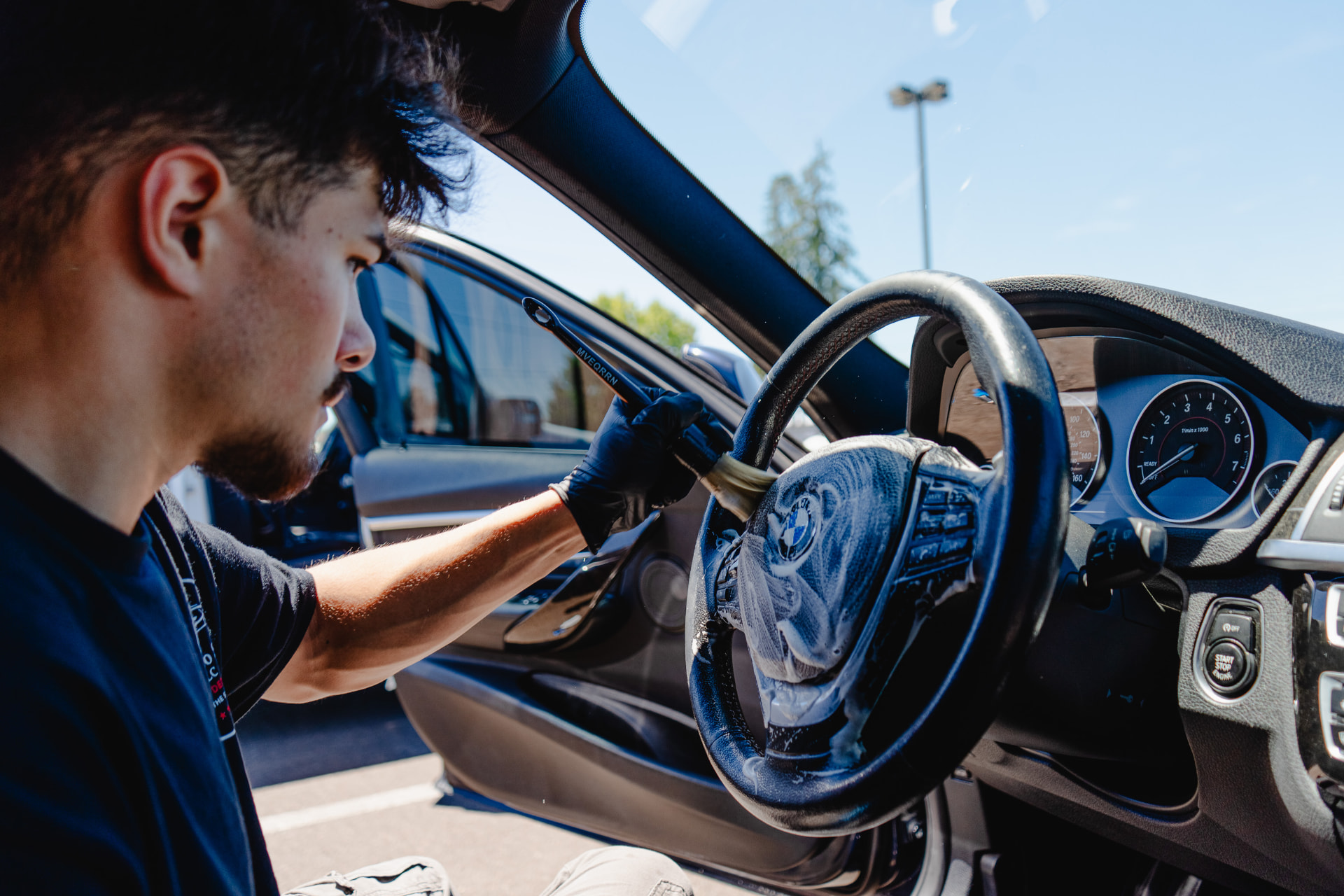 Detailer cleaning a foamed steering wheel inside a sedan